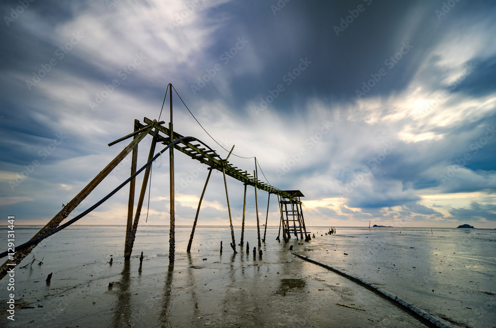Golden Hour moment,amazing tropical sunset background, wooden water pump tower on the muddy beach. cloudy and yellow sky.surface level shot.low tide sea view