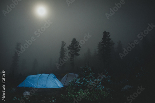 Blue tent with travelers in the mountain. Camping and tent under the forest in the fog