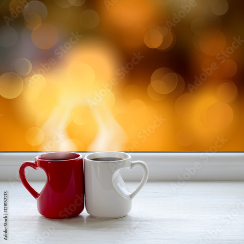 Two cups of coffee on the window sill. In the background the bright lights of the city as a Christmas background