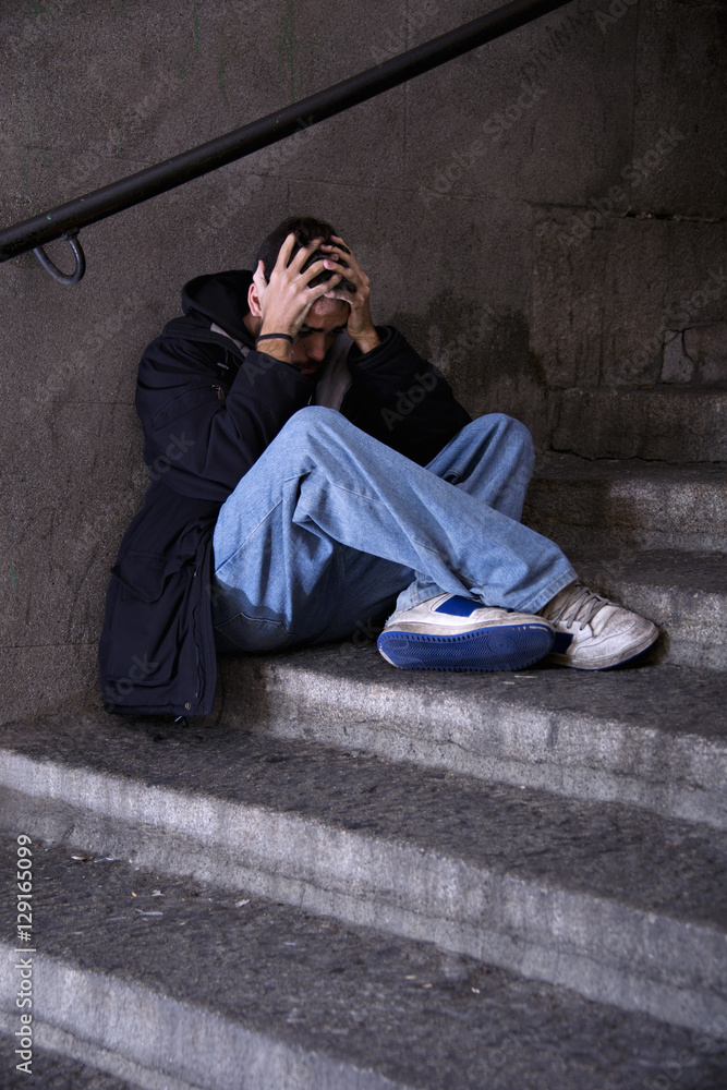 Depressed young man sitting on a public stairs Depressed young man sitting on a public stairs
