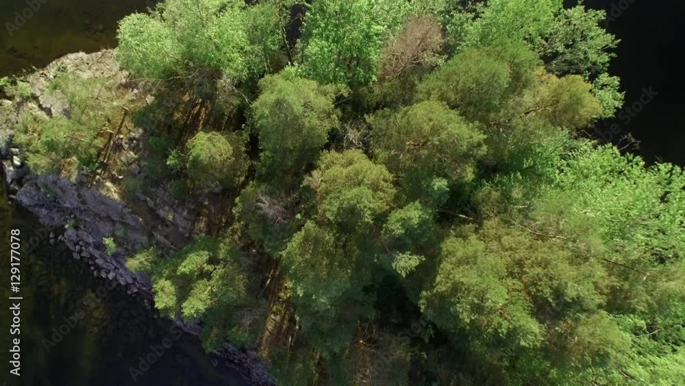 Small island with green trees and stones, rising drone shot revealing the surrounding lake. Small island with green trees and stones, rising drone shot revealing the surrounding lake.