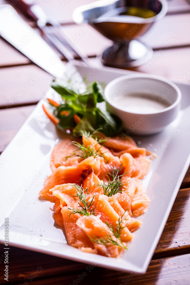 Salmon. Sliced smoked salmon with dressing and herb decoration.Serving sliced salmon in a restaurant or hotel. Salmon. Sliced smoked salmon with dressing and herb decoration.Serving sliced salmon in a restaurant or hotel.