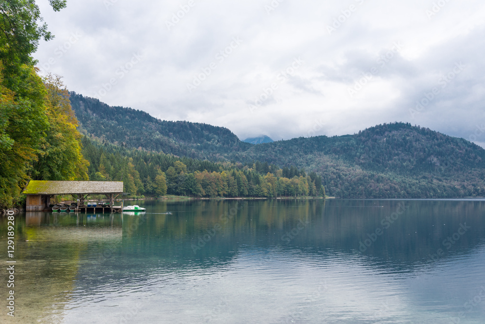 Small wood cabin on a shore of the beautiful lake name Alpsee in Bavaria, Germany during cloudy sky.