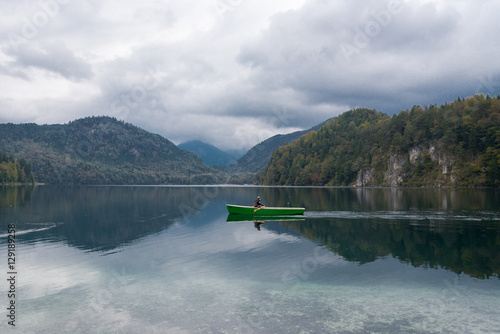 Man is kayaking on the beautiful lake name Alpsee in Bavaria, Germany during cloudy sky.