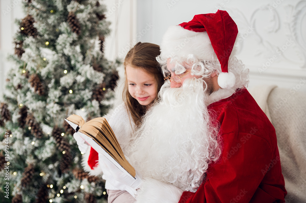 happy child girl hugging Santa reading book and laughs happy child girl hugging Santa reading book and laughs