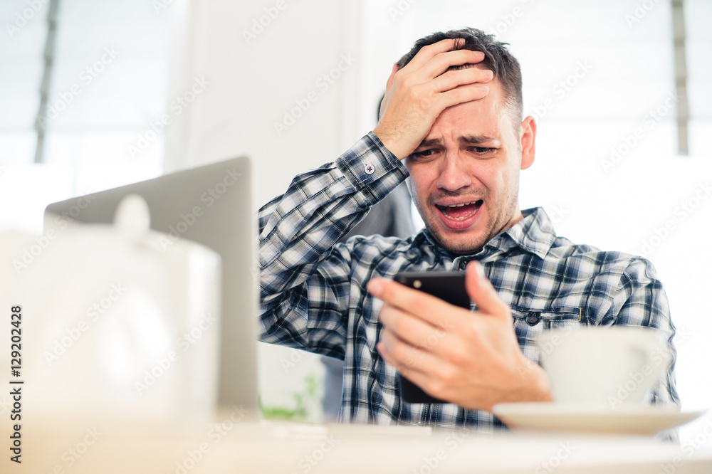 Closeup portrait, stressed young man in purple sweater, shocked surprised, horrified and disturbed, by what he sees on his cell phone, isolated indoors background. Closeup portrait, stressed young man in purple sweater, shocked surprised, horrified and disturbed, by what he sees on his cell phone, isolated indoors background.