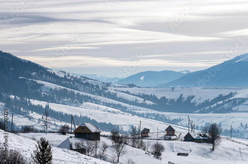 Huts in the winter mountains on a striped background of clouds in the sky. A winter landscape.