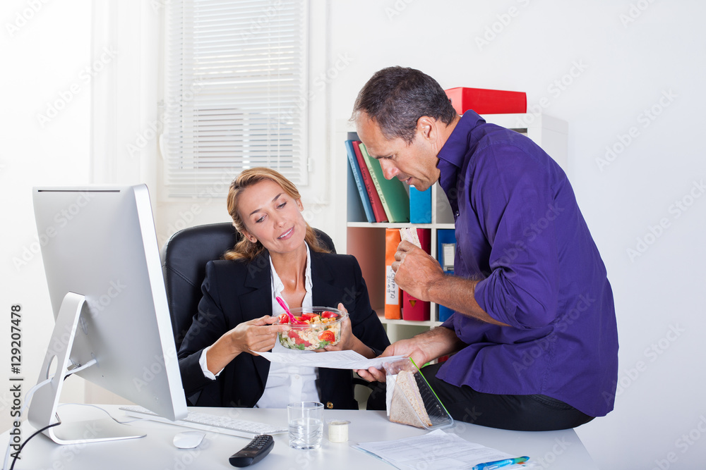couple souriant au bureau qui mange en travaillant couple souriant au bureau qui mange en travaillant