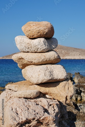 A tower of stones on Ftenagia beach at Emborio on the Greek island of Halki. The uninhabited island of Nissos is in the background.