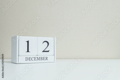 Closeup white wooden calendar with black 12 december word on blurred white wood desk and cream color wallpaper in room textured background with copy space , selective focus at the calendar