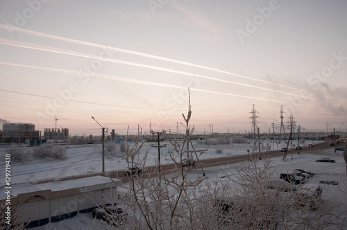 Pink sunset on the winter industrial street with prints in the sky after the airplane  View from window in the cold frosty evening. Road with cars photo