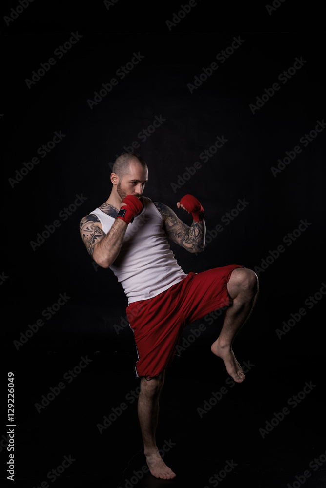 Sportsmen kick by legs. Fighting concept. Bald man with strong body in white shirt and red shorts. MMA exercising.
