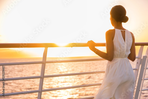 Cruise ship vacation woman enjoying sunset on travel at sea. Elegant happy woman in white dress looking at ocean relaxing on luxury cruise liner boat.