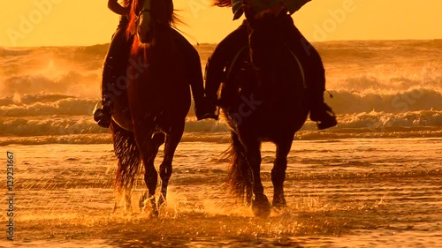Horses riding on the beach at sunset