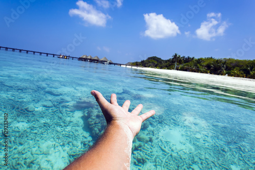 Male hand headed straight ahead appearing to touch a typical maldivian landscape with crystal clear turquoise ocean, the perfect photo for a summer holiday advertising.