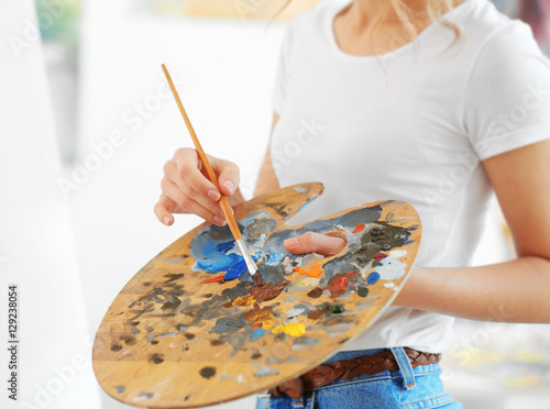 Young female artist with brush and palette in studio, close up view