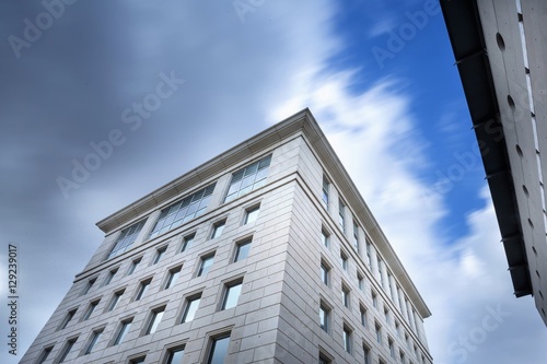 le haut d'un building blanc en contre plongée avec des nuages en mouvement