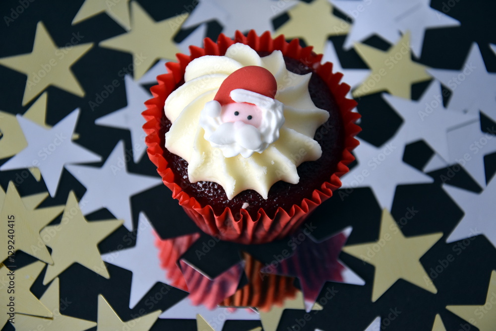 Christmas cupcake with Santa face and whipped cream topping. Xmas festive holiday food dessert. Christmas concept muffin with decoration on top and golden stars confetti background, selective focus. Christmas cupcake with Santa face and whipped cream topping. Xmas festive holiday food dessert. Christmas concept muffin with decoration on top and golden stars confetti background, selective focus.