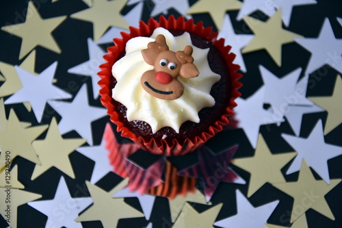 Christmas cupcake with Reindeer face and whipped cream topping. Xmas festive holiday food dessert. Christmas concept muffin with decoration on top, golden stars confetti background, selective focus. © katacarix