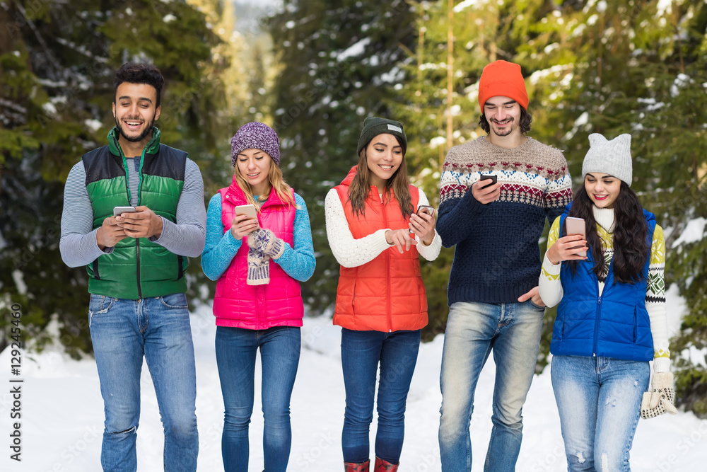 Fototapeta premium People Group Using Smart Phone Chatting Online Snow Forest Happy Smiling Young Friends Walking Outdoor Winter Pine Woods