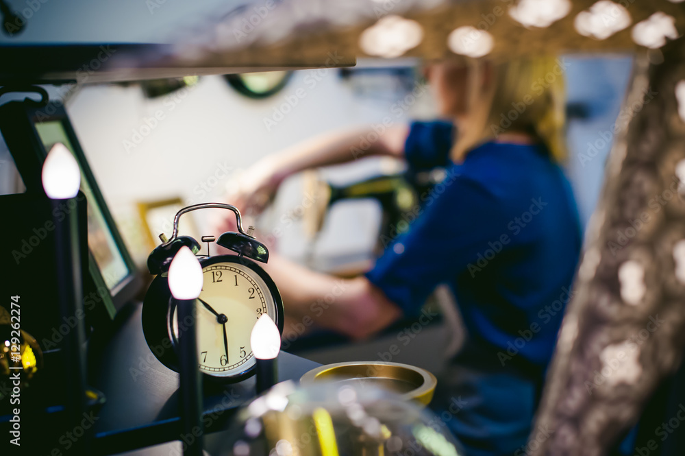 round the clock on a blurred background. seamstress work on the sewing machine. young blond woman working on a mechanical sewing machine at home sitting at your desk, be prepared to sew round the clock on a blurred background. seamstress work on the sewing machine. young blond woman working on a mechanical sewing machine at home sitting at your desk, be prepared to sew