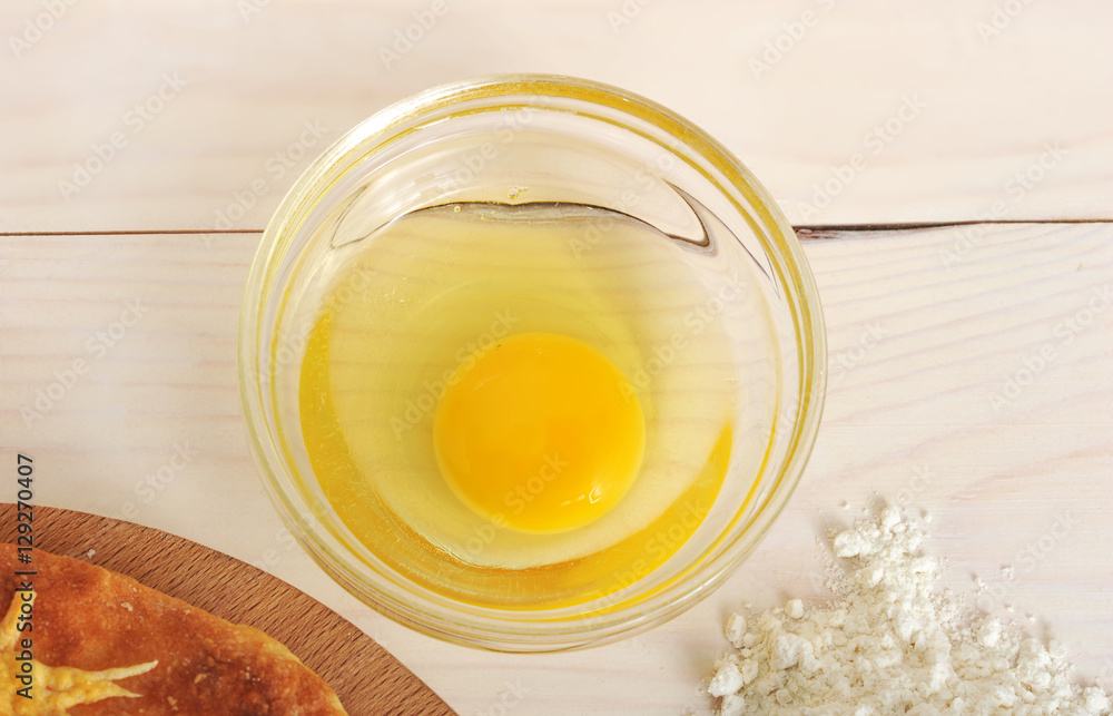 raw broken egg in a glass container on wooden background raw broken egg in a glass container on wooden background
