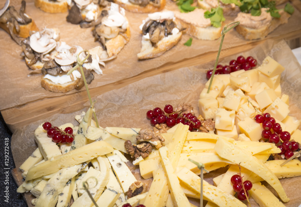 Fototapeta premium Cheese plate served with berries and nuts on a paper surface and wooden background