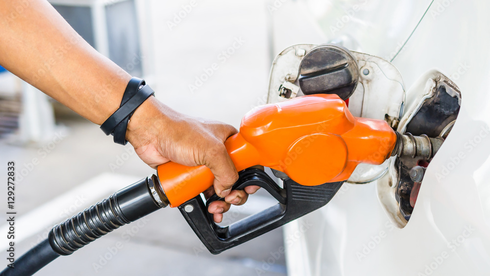 Closeup hand pumping Fuel nozzle gasoline fuel in white car at g Closeup hand pumping Fuel nozzle gasoline fuel in white car at g