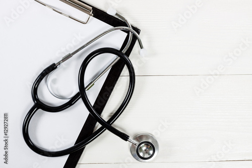 Medical clipboard and stethoscope on white wooden table