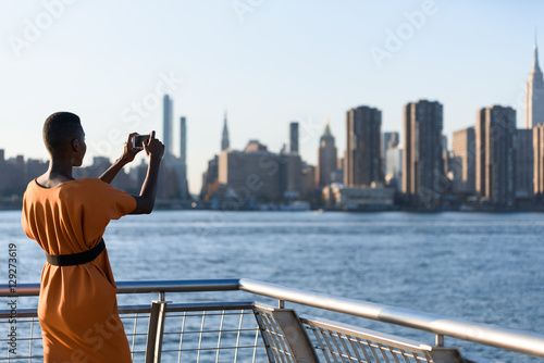 Fototapeta Naklejka Na Ścianę i Meble -  African business woman taking picture on the phone outdoor, New York, Manhattan, skyline view