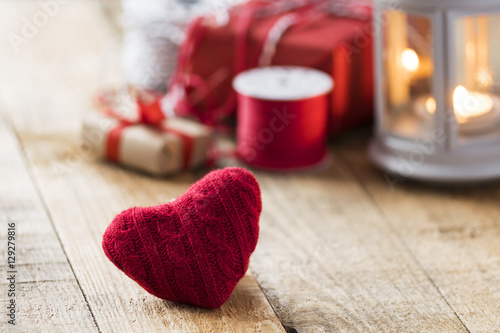 minimalistic close up view of knitted red heart on wooden desk with little present, candle and red tape for valentine's day