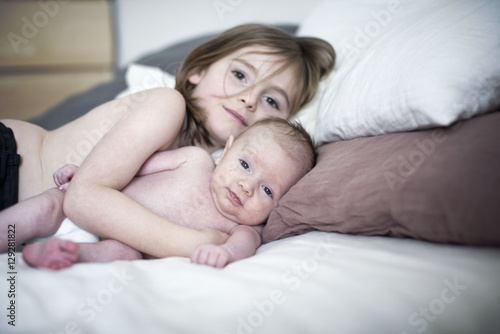 Little girl lying on bed with baby brother