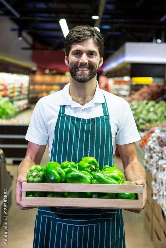 Fototapeta premium Smiling male staff holding green bell pepper