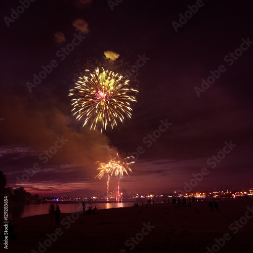 People watching colorful fireworks above the river.