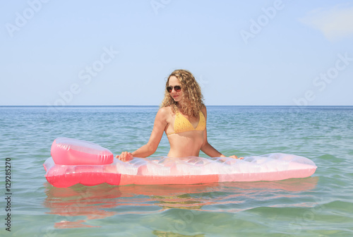 Beautiful young girl floating on a mattress in the sea