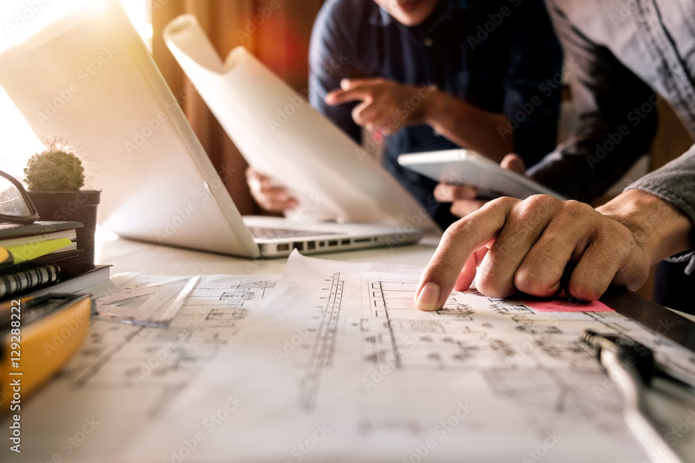 Two colleagues discussing data working and tablet, laptop with on on architectural project at construction site at desk in office Two colleagues discussing data working and tablet, laptop with on on architectural project at construction site at desk in office