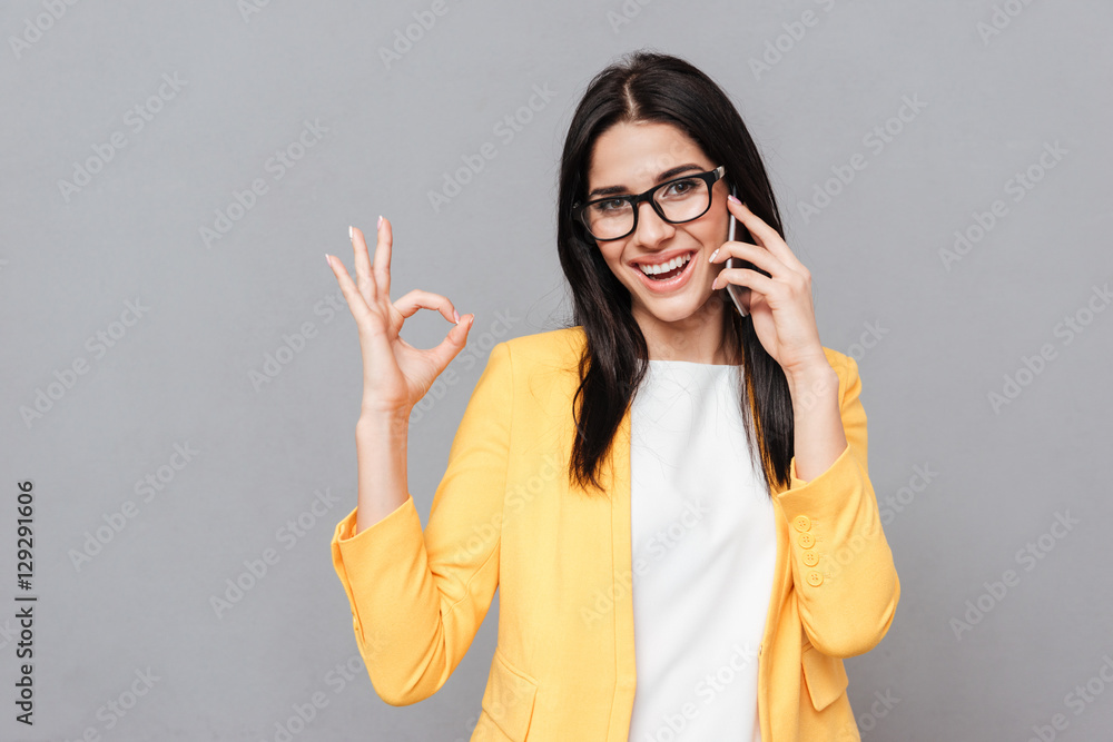 Charming young woman make Okay gesture while talking by phone Charming young woman make Okay gesture while talking by phone