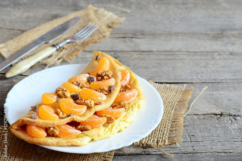 Sweet fried omelette with tangerines, walnuts and chocolate on a plate. Fork, knife, burlap textile on the old wood background with copy space for text. Healthy vegetarian omelette dessert