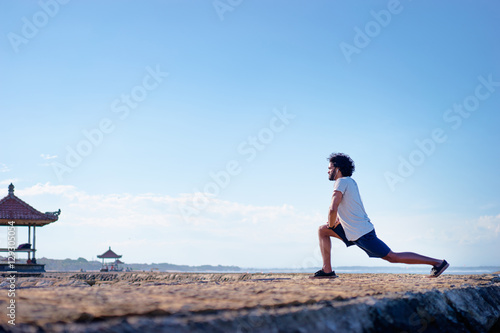 Sports lifestyle. Happy young african man stretching on the sea shore.
