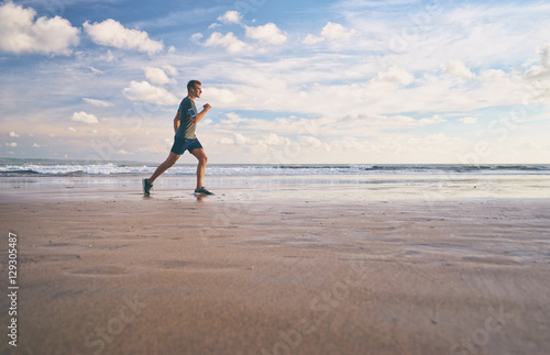 Enjoying sports lifestyle. Happy young man in headphones jogging on the sea shore.