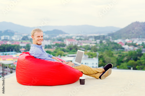 Freelance businessman. Young handsome man working on laptop while sitting on the roof top.