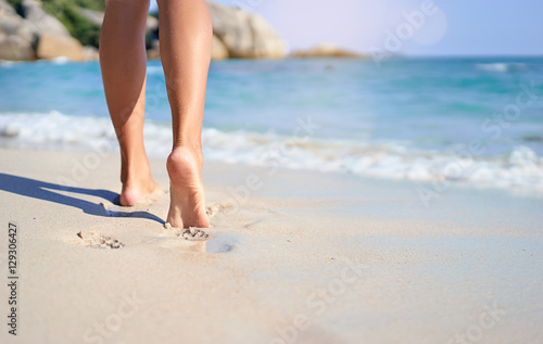 Vacation concept. Close up of female legs walking by the beach.