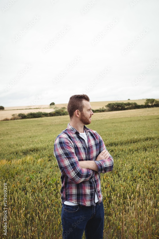 Thoughtful farmer standing with arms crossed in the field