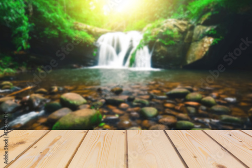 ooden board empty table in front of blurred background. Perspective brown wood over waterfall and creek in deep forest with flare of sun light   for mock up  display  montage your products  vintage. 