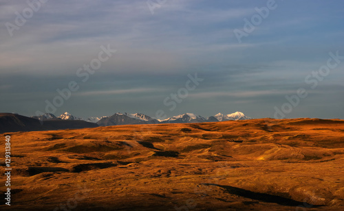 Snowcapped high ice snow mountain peaks with glaciers above orange steppe relief with under dramatic dawn sunset sky Altai Mountains Plateau Ukok Siberia Russia