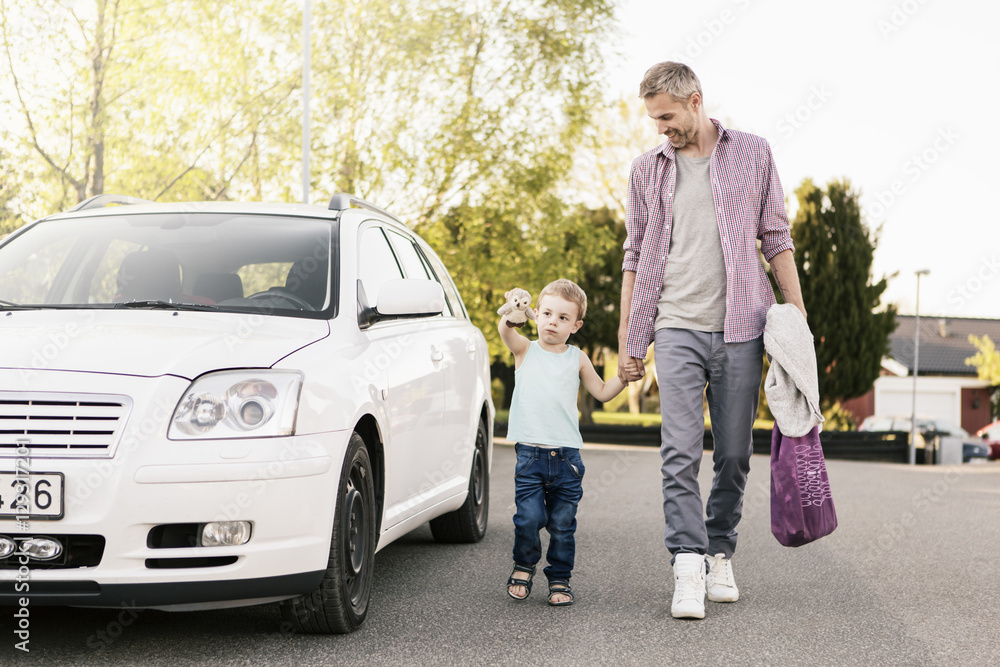 Smiling father looking at son playing with stuffed toy while walking by car on street Smiling father looking at son playing with stuffed toy while walking by car on street