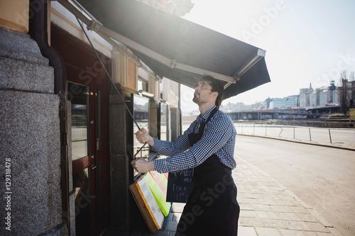 Male owner turning crank handle for winding out awning at fish store photo