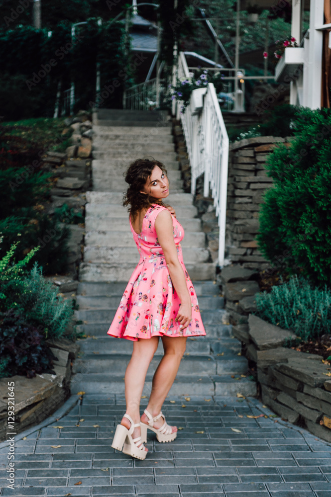 Beautiful brunette girl posing in pink dress outside near tropical plants Beautiful brunette girl posing in pink dress outside near tropical plants