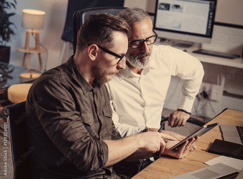 Closeup view of business people meeting process.Bearded man showing startup idea on mobile tablet.Adult businessman working together with young partner at the wooden table.Horizontal,blurred. Closeup view of business people meeting process.Bearded man showing startup idea on mobile tablet.Adult businessman working together with young partner at the wooden table.Horizontal,blurred.