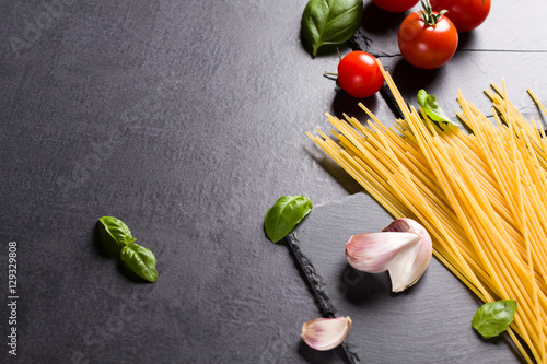 Food ingredients for Italian spaghetti on black stone slate background with much copy space of your project.